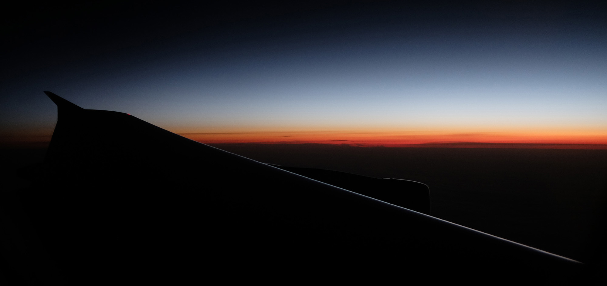 The sun sets behind the wing of an airliner.